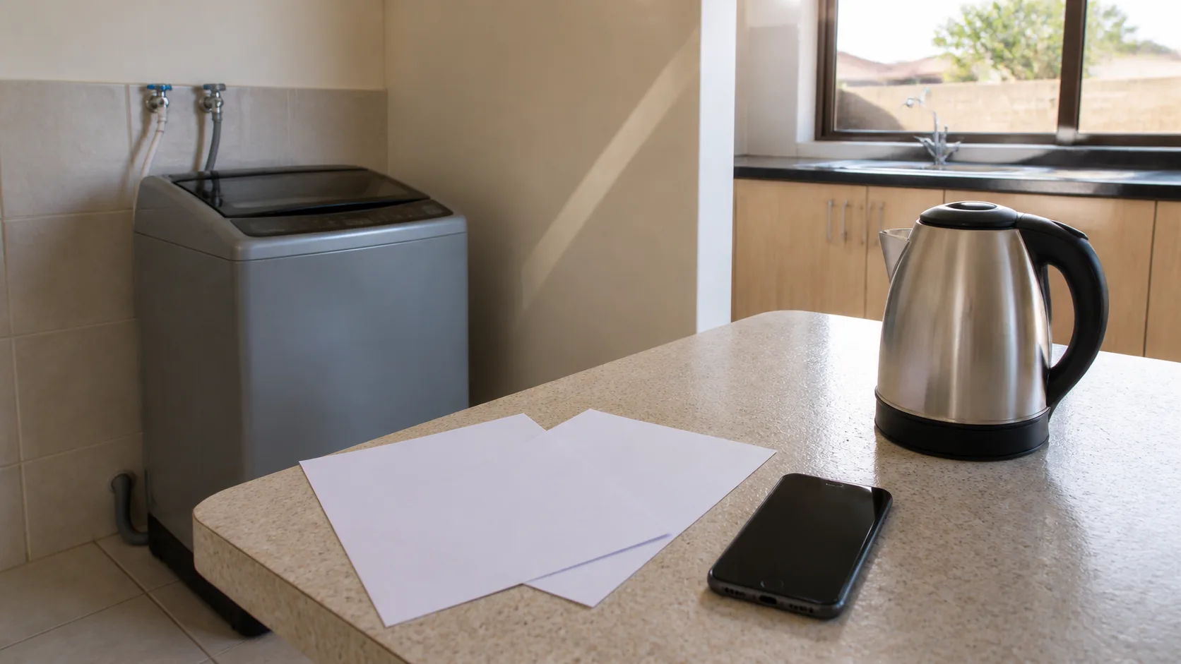 Unbranded washing machine, kettle and smartphone arranged with blank catalogue sheets on a Gaborone worktop.